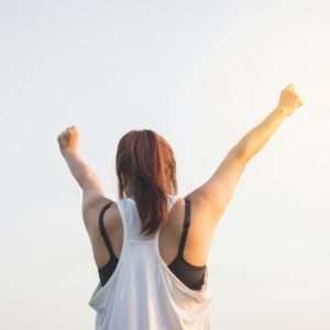 A woman celebrates success with arms raised in a bright outdoor setting.