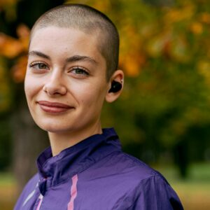 Portrait of a woman with a buzzcut wearing earbuds outdoors in autumn.